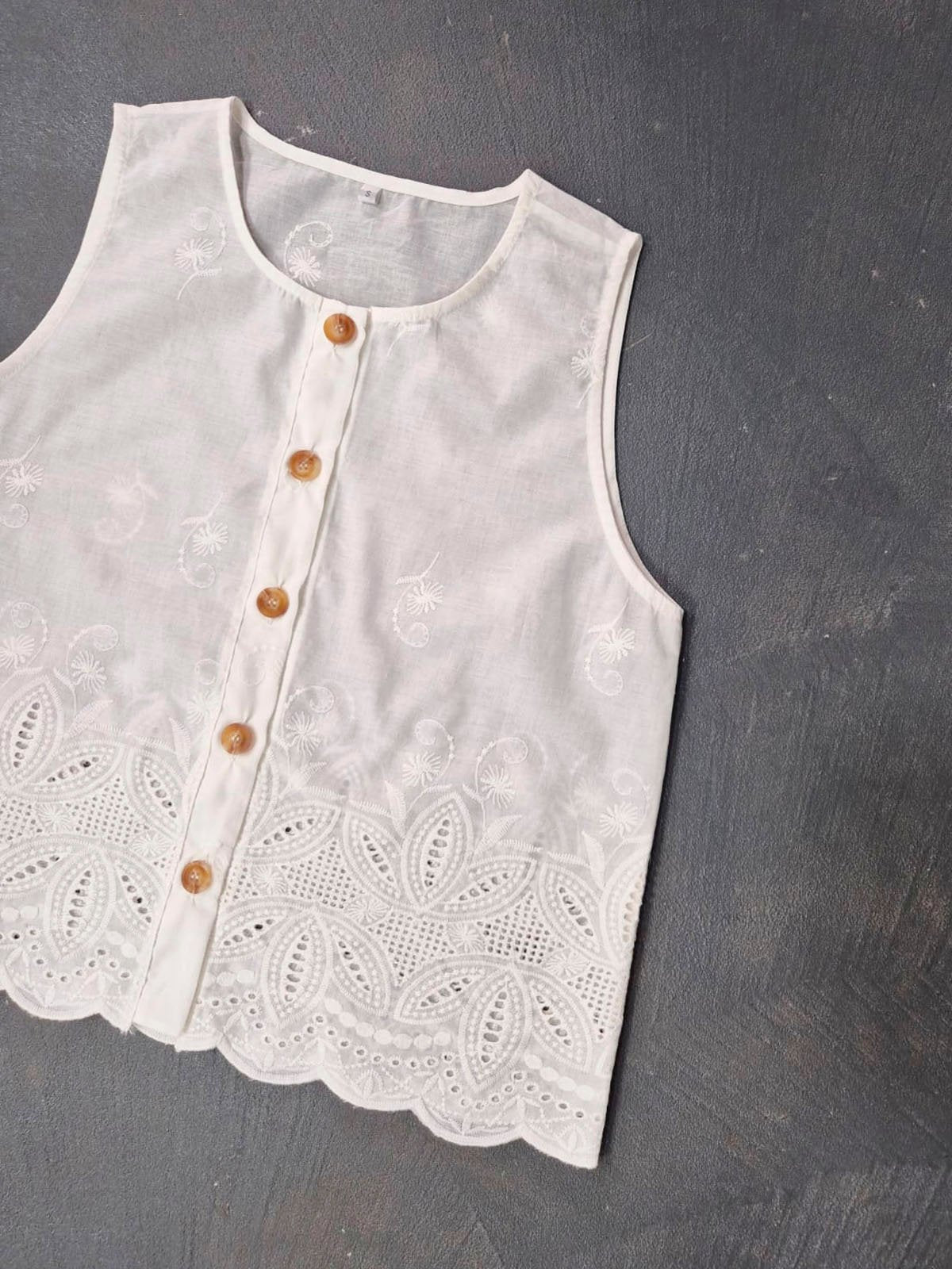 Blusa blanca sin mangas con bordado inglés y botones de madera