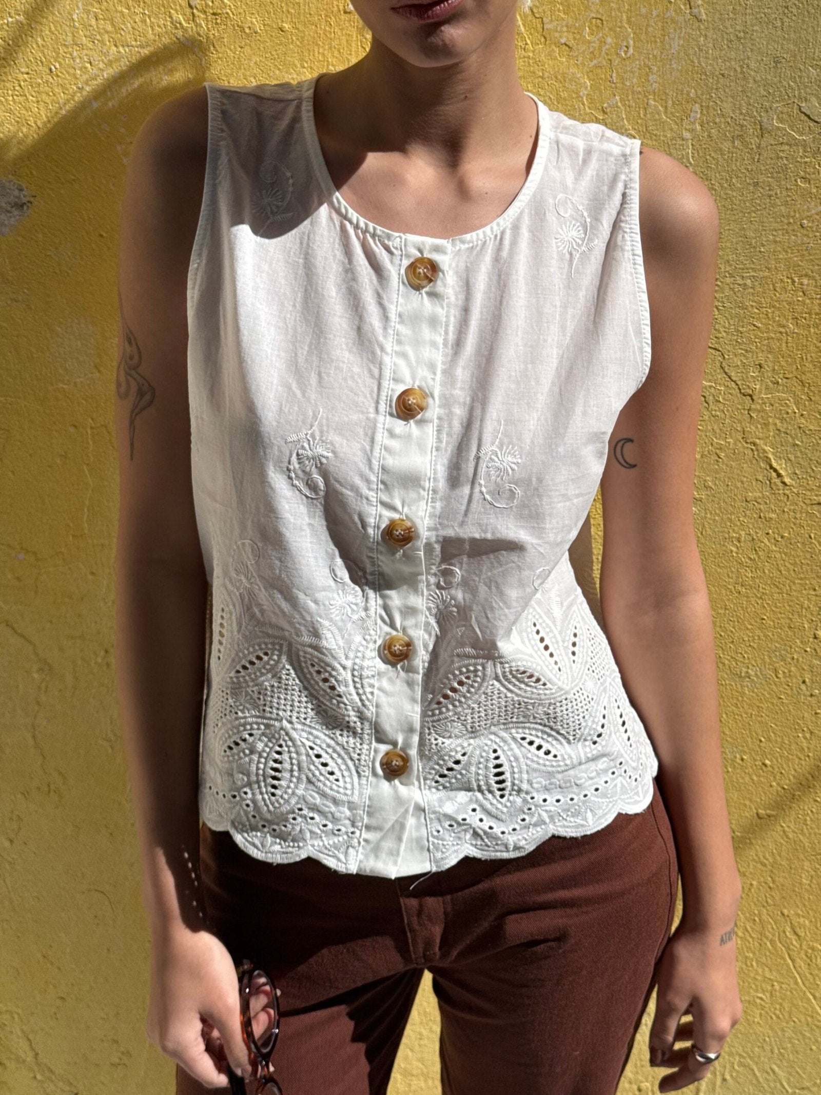 Blusa blanca sin mangas con botones dorados y encaje en borde inferior