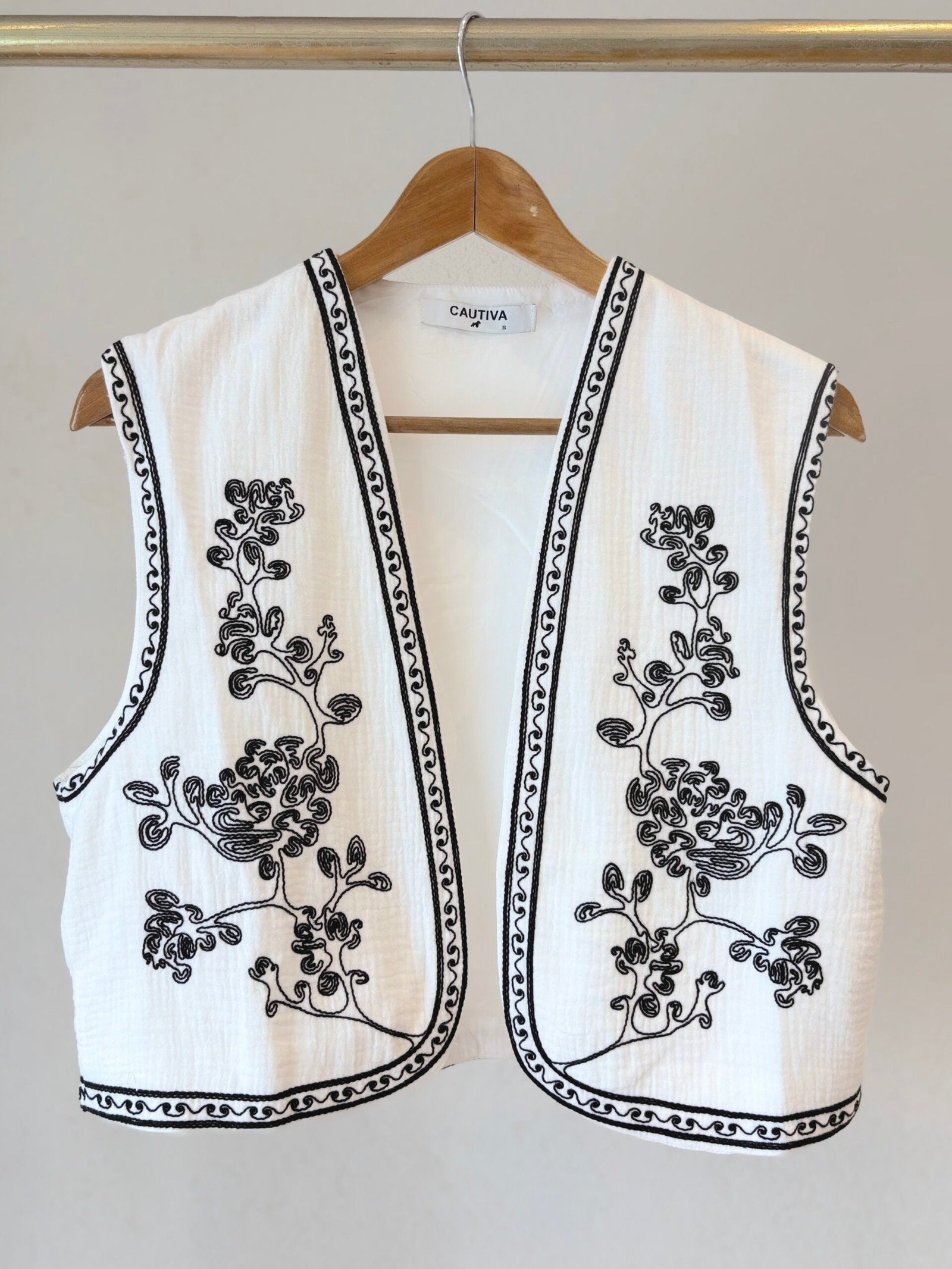 Chaleco blanco sin mangas con bordado floral negro y ribete decorativo