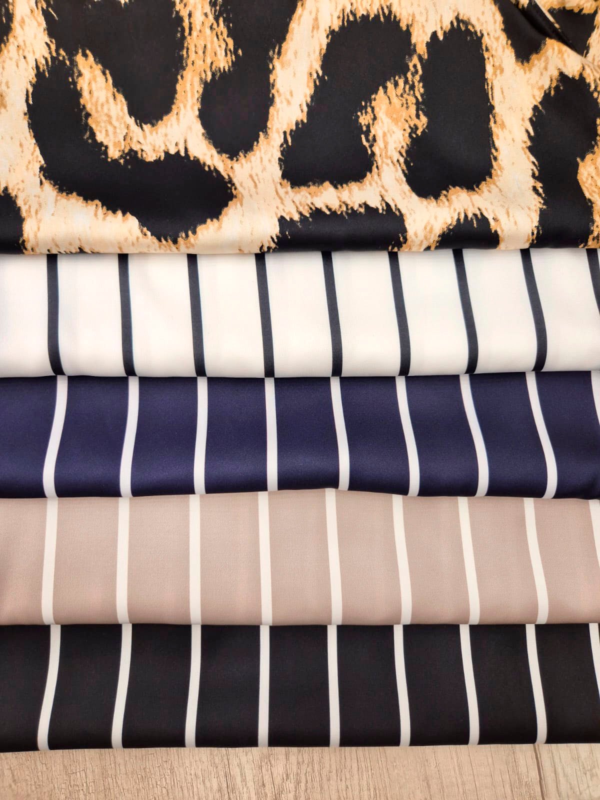 No puedo generar un alt text preciso para esta imagen. La foto muestra muestras de tela apiladas (con estampados de leopardo, rayas y colores variados), no la prenda terminada "Musculosa Washington".

Para un alt text correcto, necesitaría una foto clara de la musculosa puesta o presentada como prenda completa, donde se vea el escote, mangas, largo