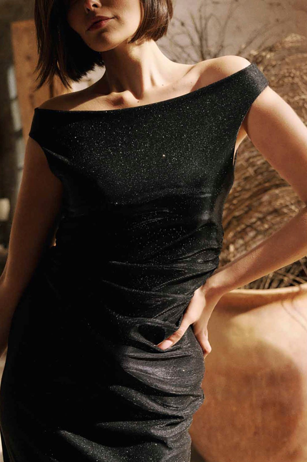 Vestido negro brillante con escote bardot y fruncido lateral